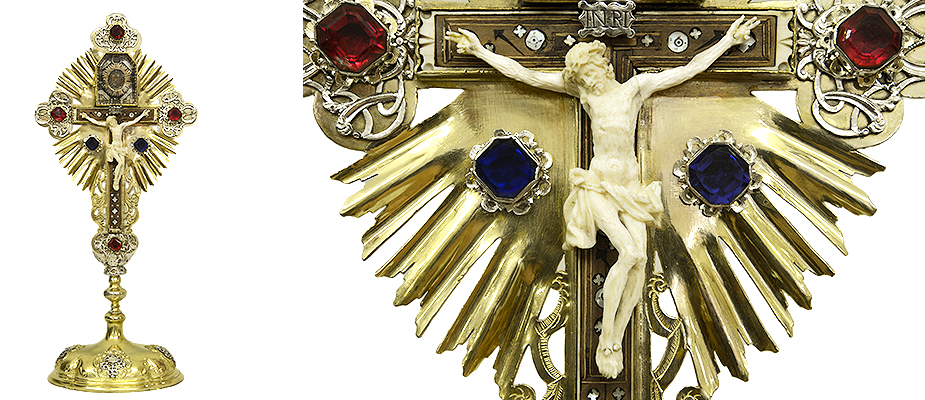 StandkreuzSueddeutsch Tabernakelkreuz, Messing, feuervergoldet und versilbert. Der Standfuß ornamental getrieben. Das Kreuz aus Jerusalem mit Perlmutteinlagen. Der Christus in Bein geschnitzt. Der Kreuzpartikelbehälter aus Messing, feuervergoldet und facettierten Glas. Der Strahlenkranz der Kreuzreliquie, Messing feuervergoldet. Die Reliquie rückseitig mit Siegel. Das Standkreuz mit eingefassten, facettierten, bunten Glassteinen besetzt. Maße: H 48 x B 21 x T 14,5 cm Bayern Barock, Mitte 18. Jahrhundert